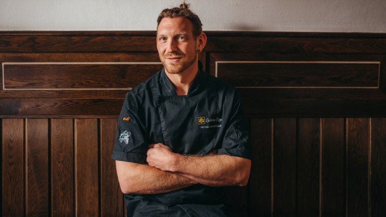 Landlord Michael Schindler, © Niederösterreich Werbung/Daniela Führer A man in a black chef's jacket sits in front of a wooden wall.