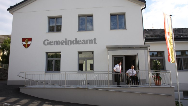 Gemeindehaus, © Marktgemeinde Sallingberg Ein modernes Gemeindeamt mit weißer Fassade, zwei Personen stehen auf einer Rampe, daneben weht eine Flagge.