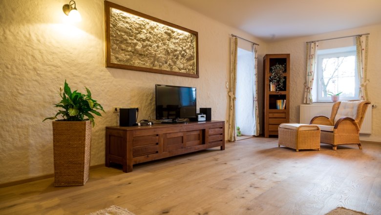 Landhaus Lunkowitz, © Benjamin Butschell Gemütliches Wohnzimmer mit Holzmöbeln, Fernseher, Rattansessel und Pflanzen.