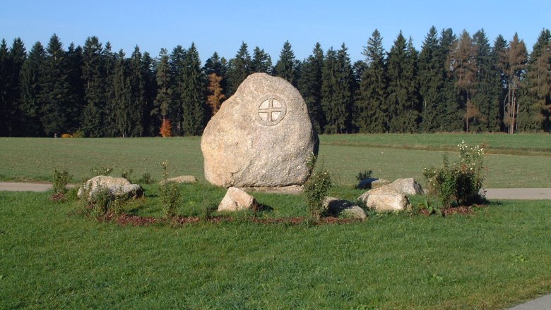 Marktgemeinde Großgöttfritz, © Marktgemeinde Großgöttfritz Großer Stein mit eingraviertem Symbol auf einer Wiese, umgeben von kleineren Steinen und Pflanzen, im Hintergrund ein Wald.