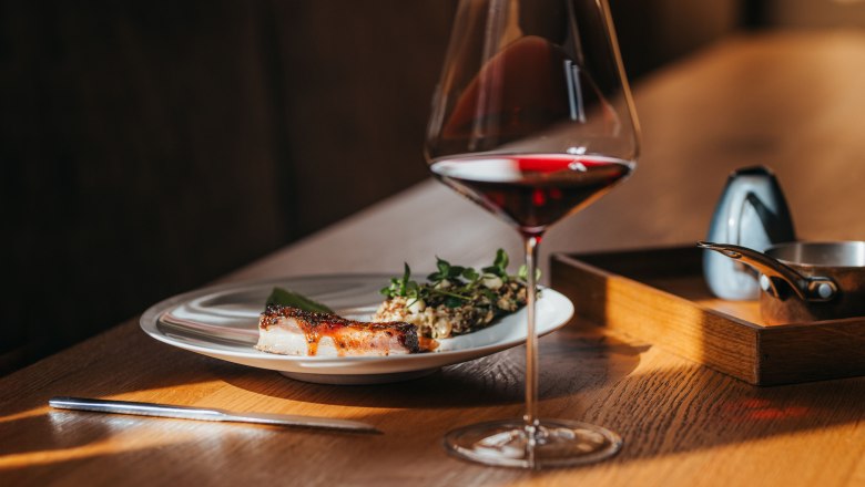Lamb belly, lettuce & wasabi cream, © Niederösterreich Werbung/Daniela Führer A plate of lamb belly, lettuce and wasabi cream next to a glass of red wine on a wooden table.