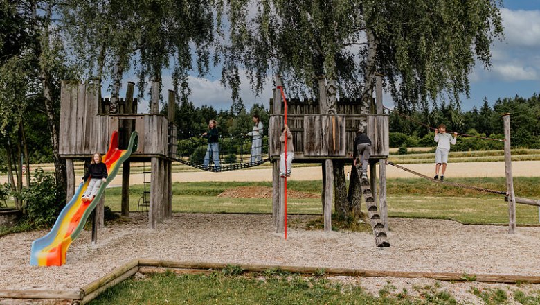 Spielplatz, © Waldviertel Tourismus, Matthias Streibel Kinder spielen auf einem hölzernen Spielplatz mit Rutsche und Seilbrücke im Freien.