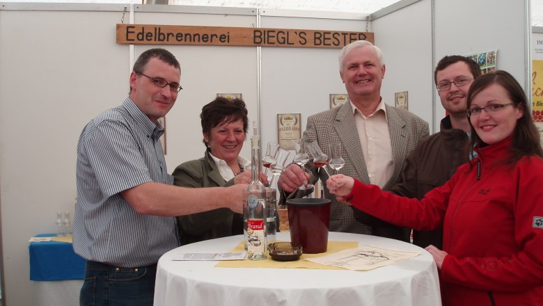 Edelbrennerei Bernhard & Sabine Biegl, © Edelbrennerei Bernhard & Sabine Biegl Gruppe von fünf Personen stößt mit Gläsern an einem Tisch an.