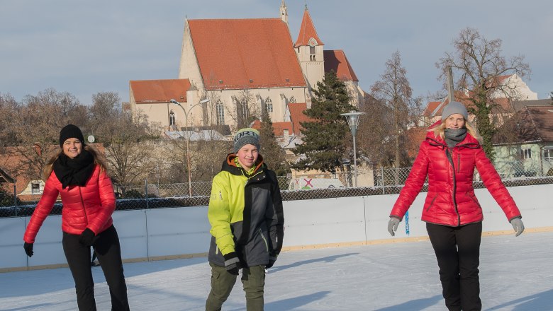 Ice rink in Eggenburg, © Jarmer Margarete Three people skating on an ice rink with a church in the background.
