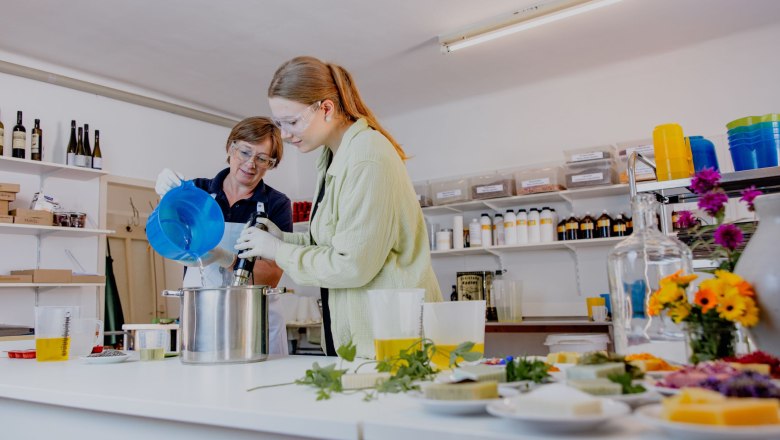 Seifen sieden, © Waldviertel Tourismus, Matthias Streibel Zwei Personen arbeiten in einer Werkstatt an einem Topf mit Flüssigkeiten und Kräutern auf einem Tisch. Sie produzieren Seifen.