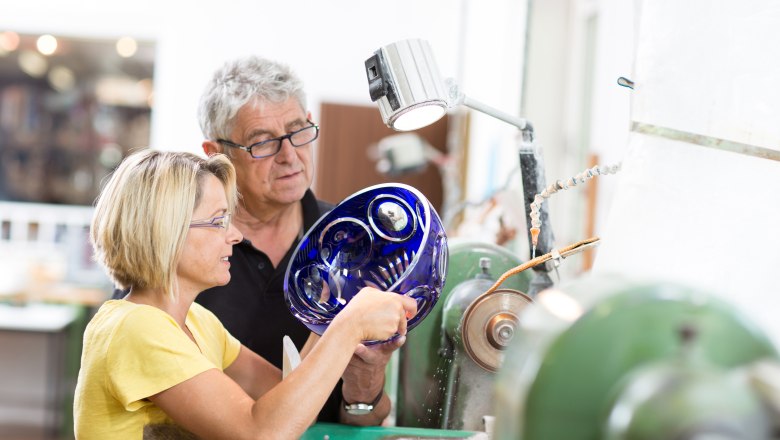 Zwei Personen arbeiten an einer Glasschleifmaschine mit einer blauen Glasschale.