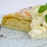 A slice of white poppy seed and pear strudel with cream and mint leaf on a plate.