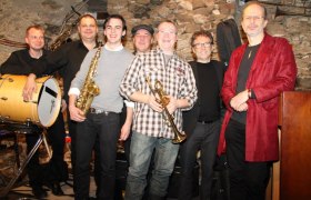Gruppe von sieben Männern mit Musikinstrumenten in einem Jazzclub.