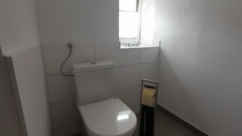Ein schlichtes Badezimmer mit Toilette, Toilettenpapierhalter und kleinem Fenster.