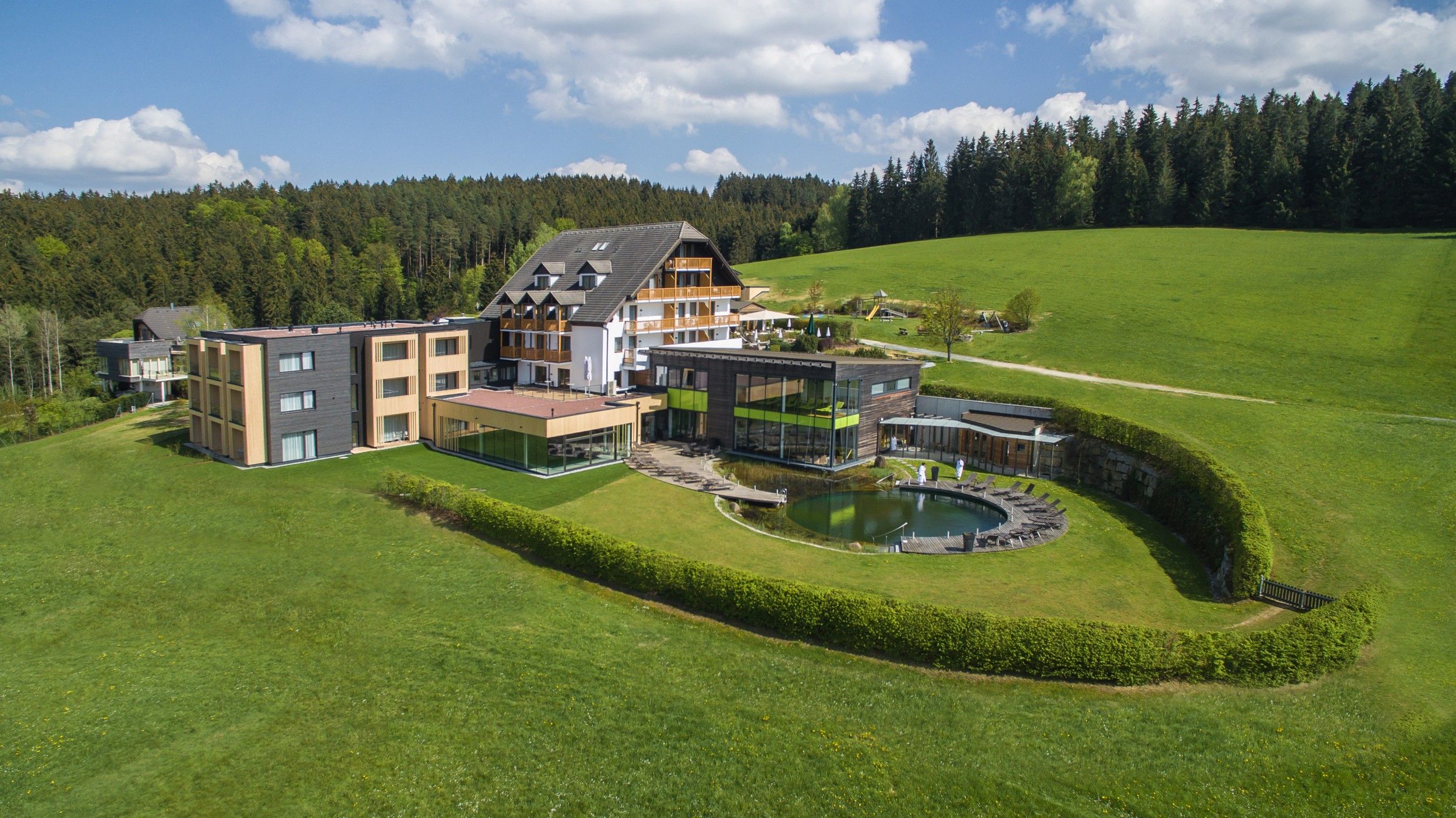 Luftaufnahme eines modernen Hotels mit Pool in grüner Landschaft.