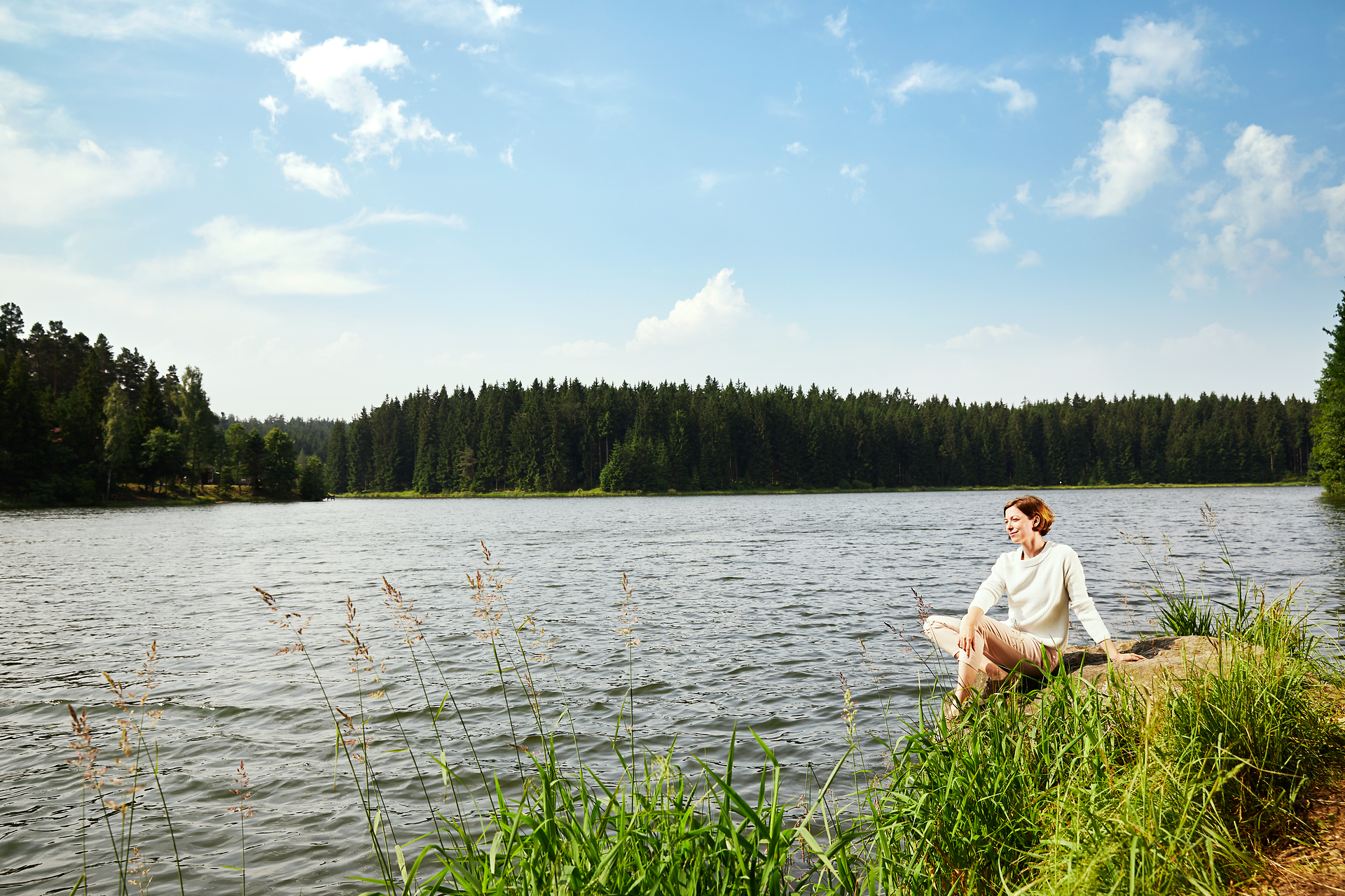 Ein ruhiger Moment am Ufer eines glitzernden Sees, umgeben von üppigen Wäldern und sanften Hügeln. Die sanfte Brise und das Zwitschern der Vögel schaffen eine friedliche Atmosphäre, die zum Entspannen einlädt. Hier in der Natur findet man die perfekte Auszeit vom Alltag.