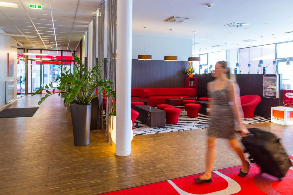 Hotel-Lobby mit rotem Sofa und Frau mit Koffer.