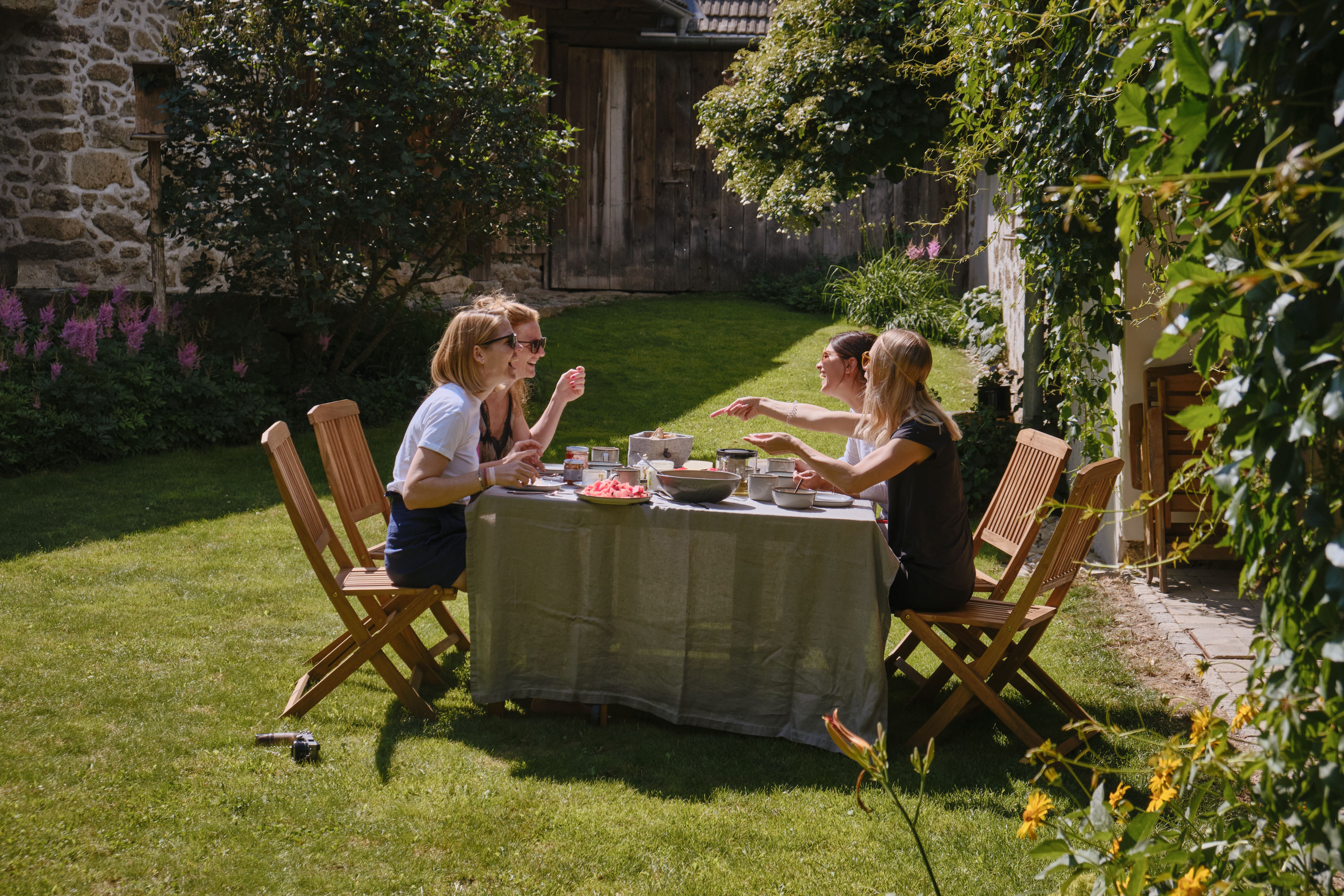 Vier Personen sitzen an einem Tisch im Garten und essen zusammen.