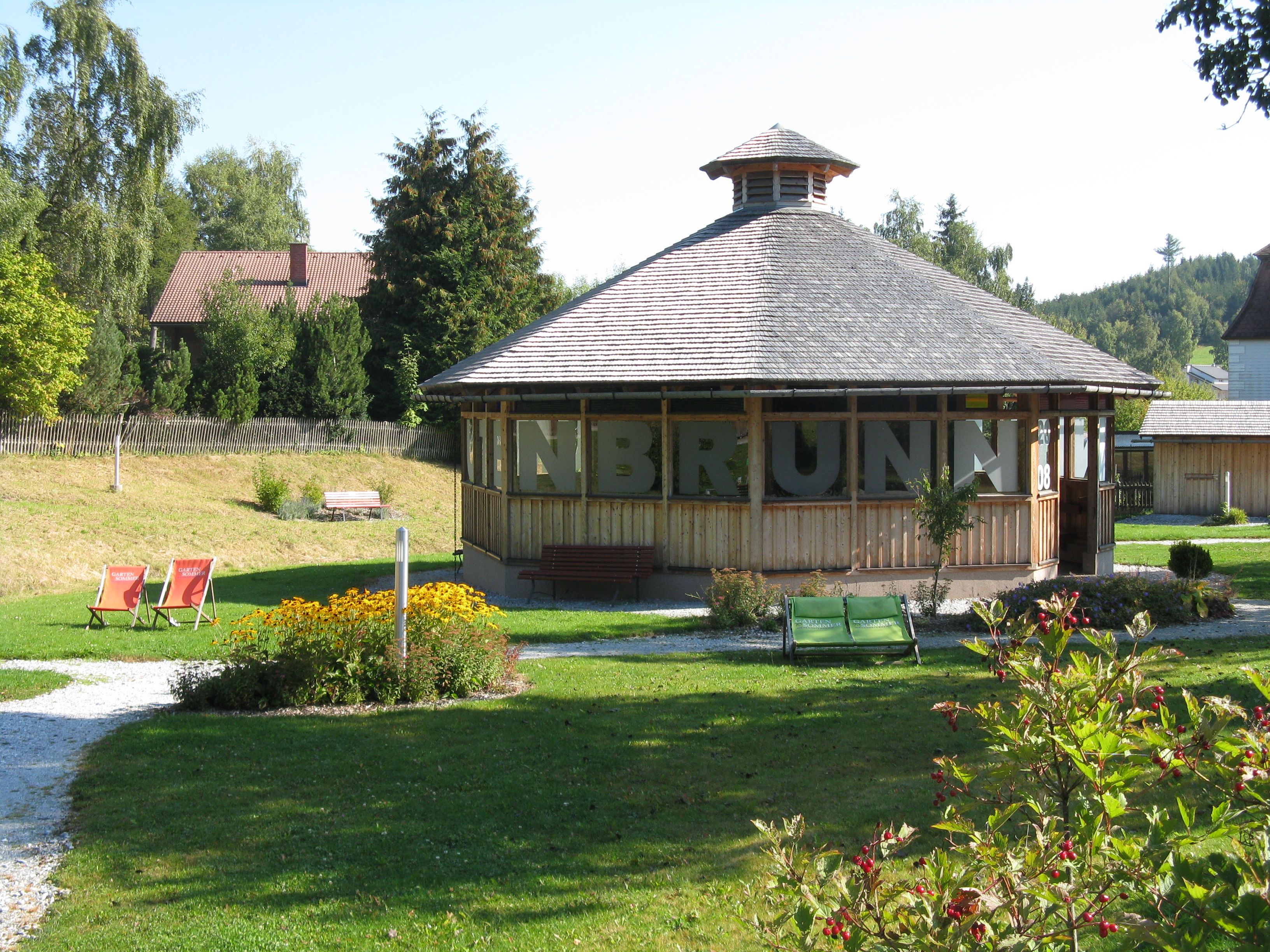 Ein rundes Gradierwerk in einem grünen Park mit Blumen und Liegestühlen.