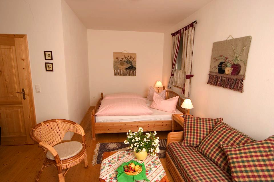 Gemütliches Gästezimmer mit Holzmöbeln, einem Bett, einem Sofa, einem Tisch mit Blumen und Obst, und Wanddekorationen.