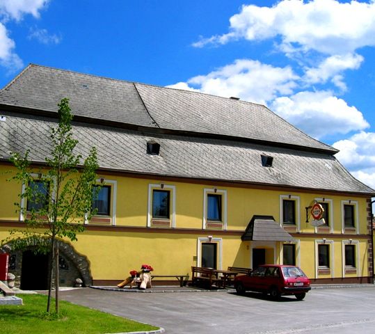 Gelbes Gasthaus mit grauem Dach und rotem Auto davor.