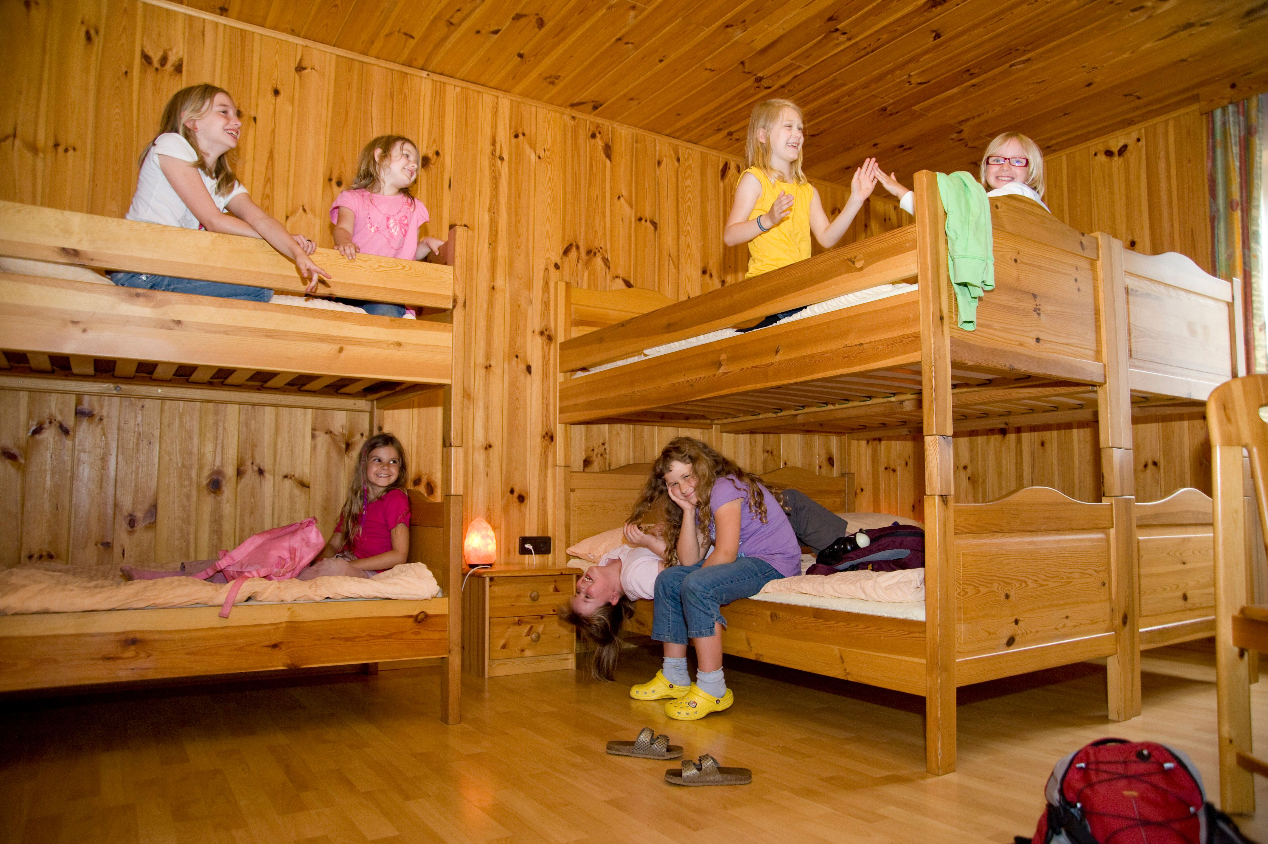 Kinder spielen in einem Zimmer mit Holzstockbetten.