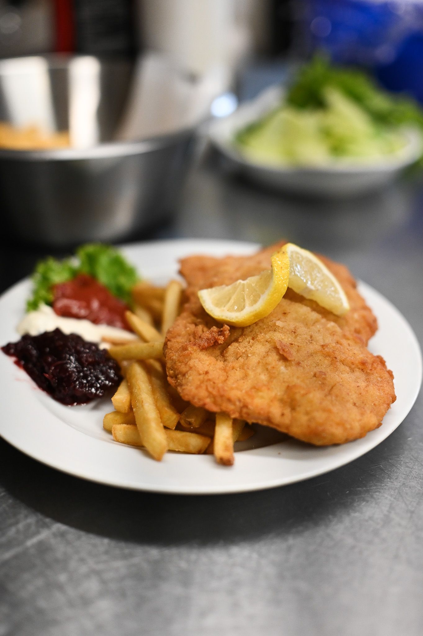 Ein Teller mit Schnitzel, Pommes frites, Zitronenscheiben und verschiedenen Soßen.