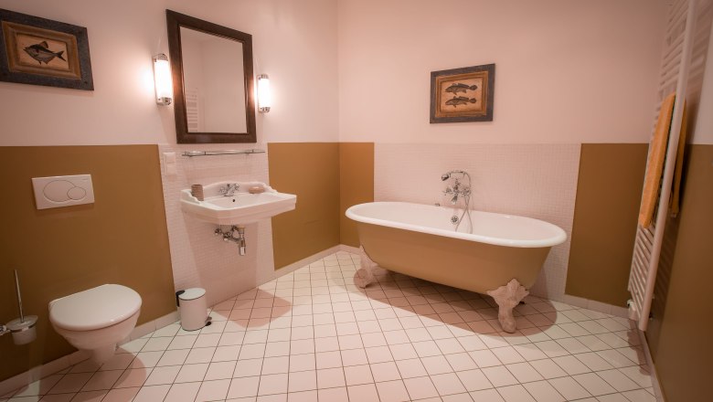 Elegantes Badezimmer mit freistehender Badewanne, Waschbecken, Spiegel und WC. Wände in Beige und Weiß, dekoriert mit Fischbildern.