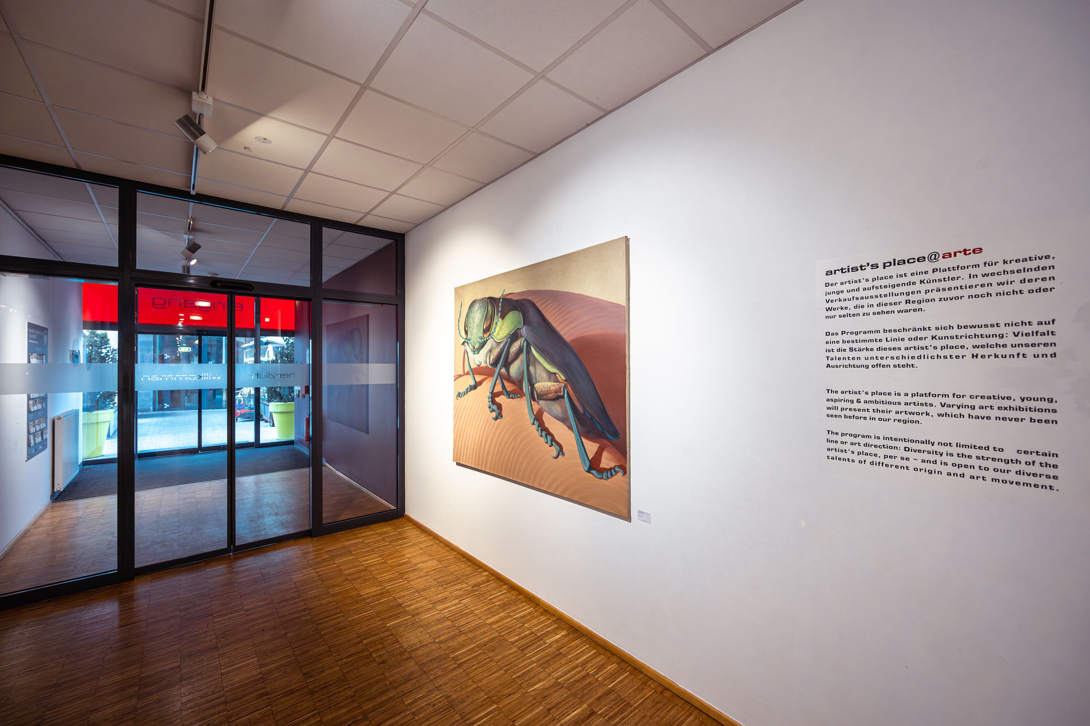 Innenansicht eines Flurs im arte Hotel Krems mit einem großen Insektenbild an der Wand und einer Glastür im Hintergrund.
