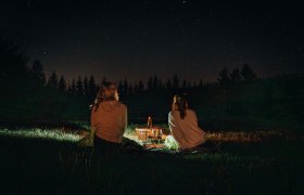 Zwei Personen sitzen nachts auf einer Wiese und schauen in den Sternenhimmel.