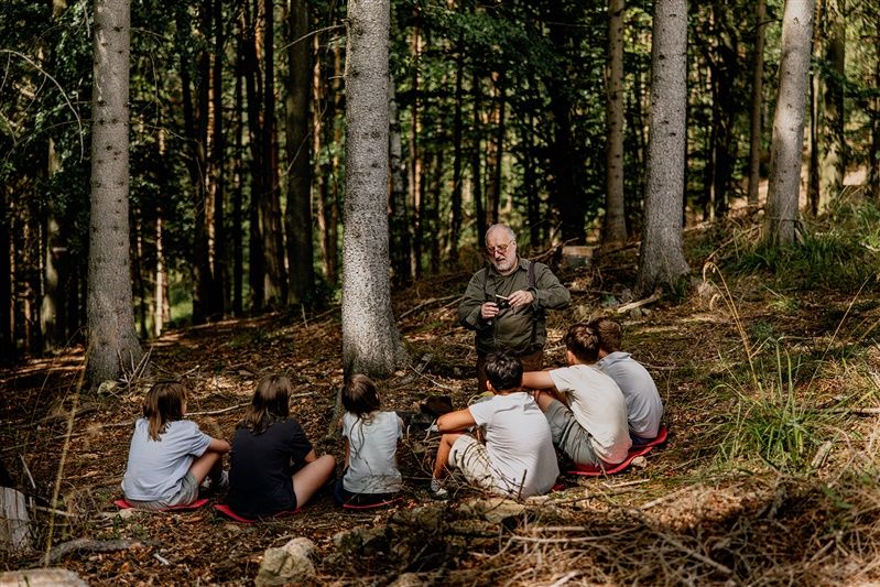 Ein älterer Mann erklärt einer Gruppe von Jugendlichen etwas im Wald.