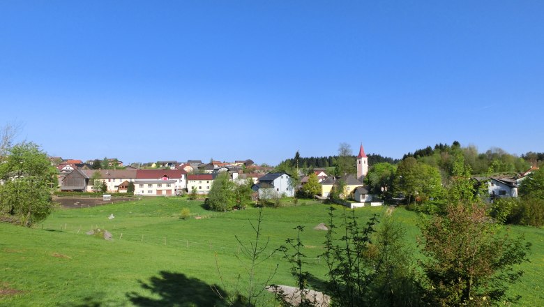 Landschaftsansicht der Marktgemeinde Altmelon mit grünen Wiesen und einer Kirche im Hintergrund.