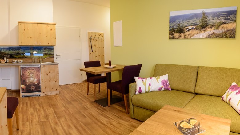 Cozy room with green couch, wooden furniture and landscape photo on the wall.
