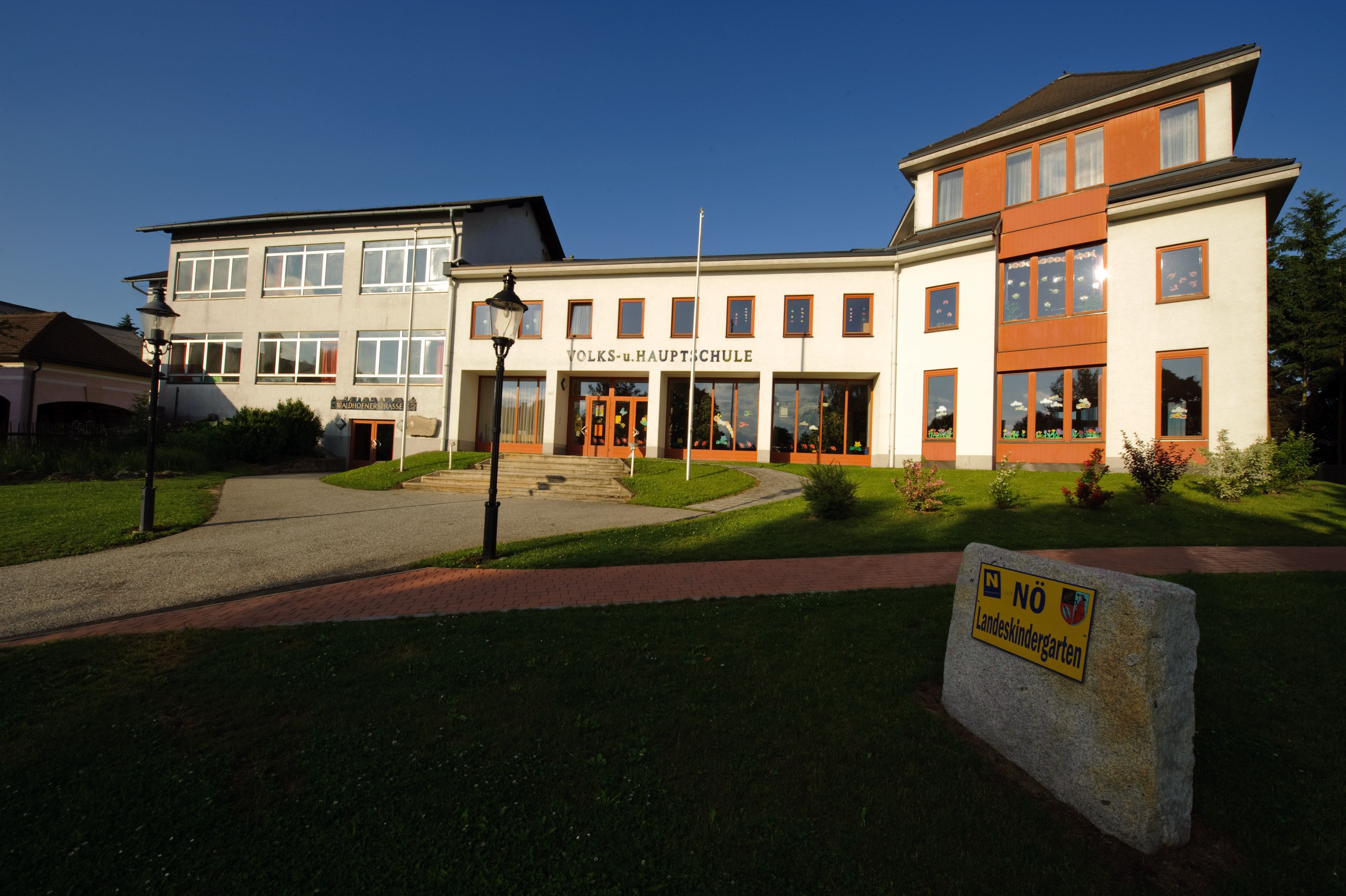 Gebäude der Volks- und Hauptschule Kautzen mit gepflegtem Rasen und einem Schild für den Landeskindergarten.