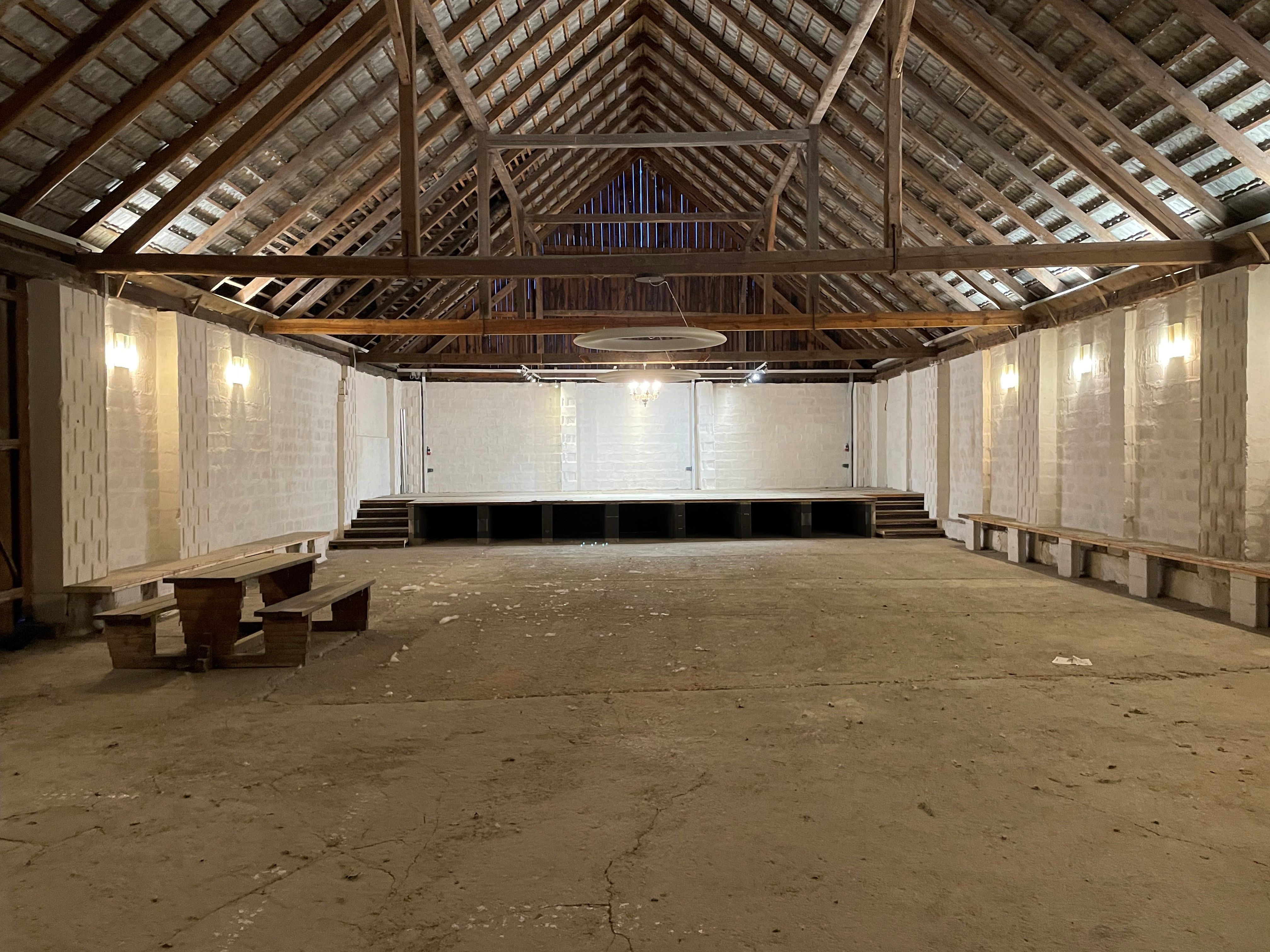 Innenansicht eines leeren Stadls mit Holzdach und Bühne.