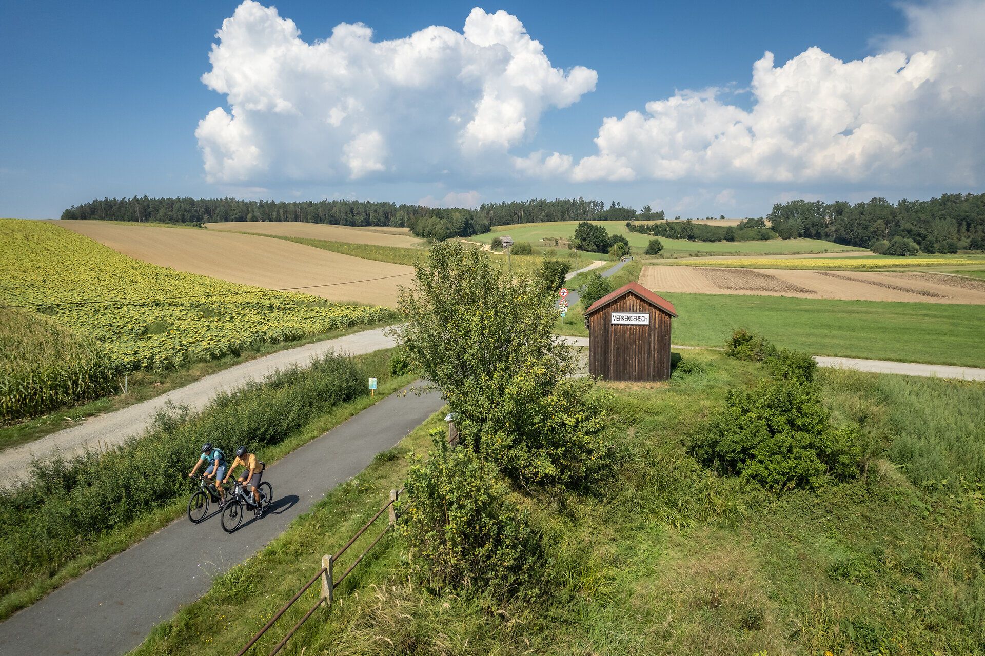 Die sanften Hügel und weitläufigen Felder laden zu einer erfrischenden Radtour ein. Radfahrer genießen die idyllische Landschaft, während die Sonne über den Horizont strahlt und die Wolken sanft am Himmel treiben. Ein perfekter Tag, um die Natur in ihrer vollen Pracht zu erleben.