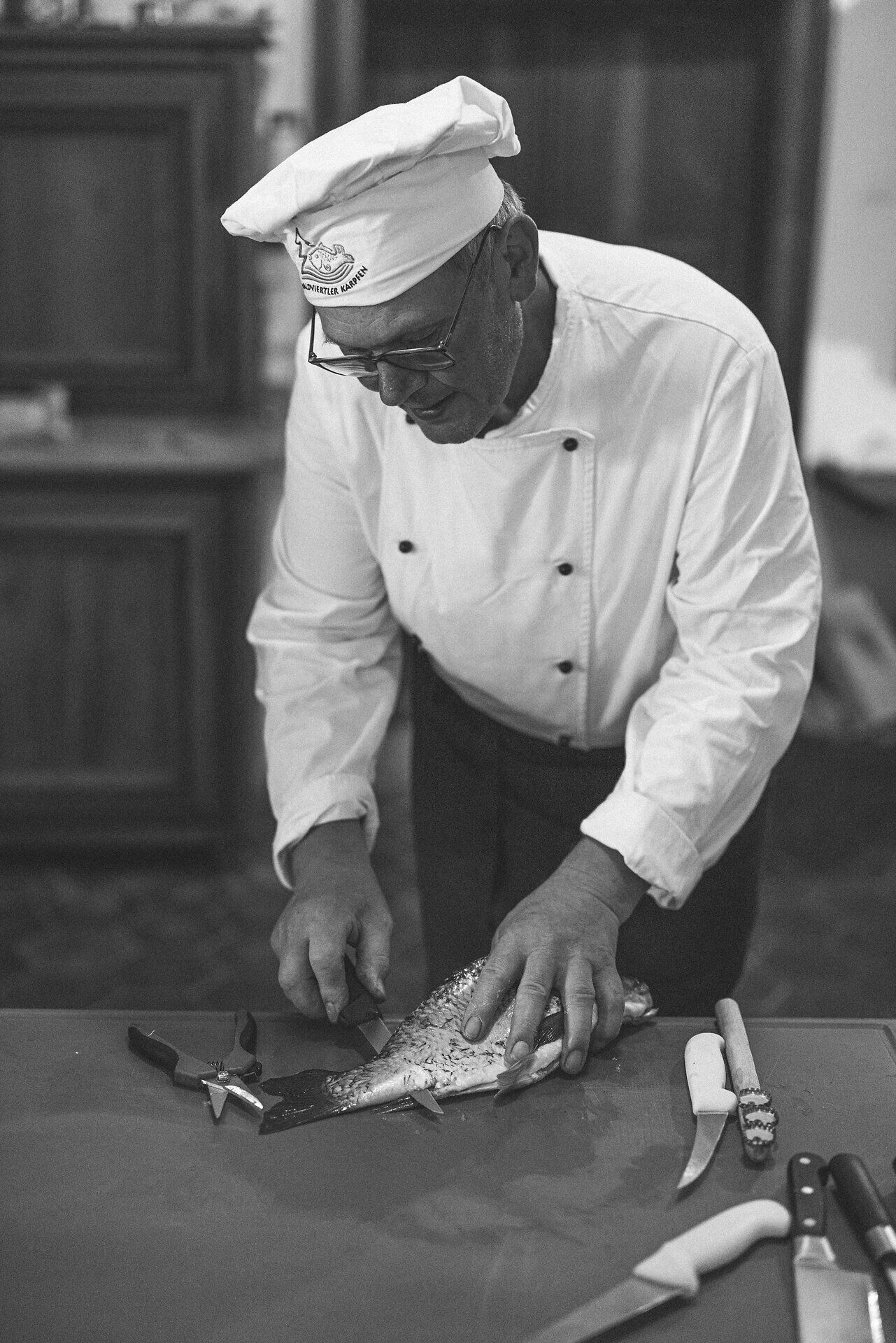 Ein erfahrener Koch bereitet mit Hingabe einen frischen Karpfen zu, während die Vorfreude auf ein köstliches Gericht in der Luft liegt. Die sorgfältige Handhabung der Werkzeuge und die Konzentration des Kochs schaffen eine einladende Atmosphäre, die die Liebe zur regionalen Küche widerspiegelt.