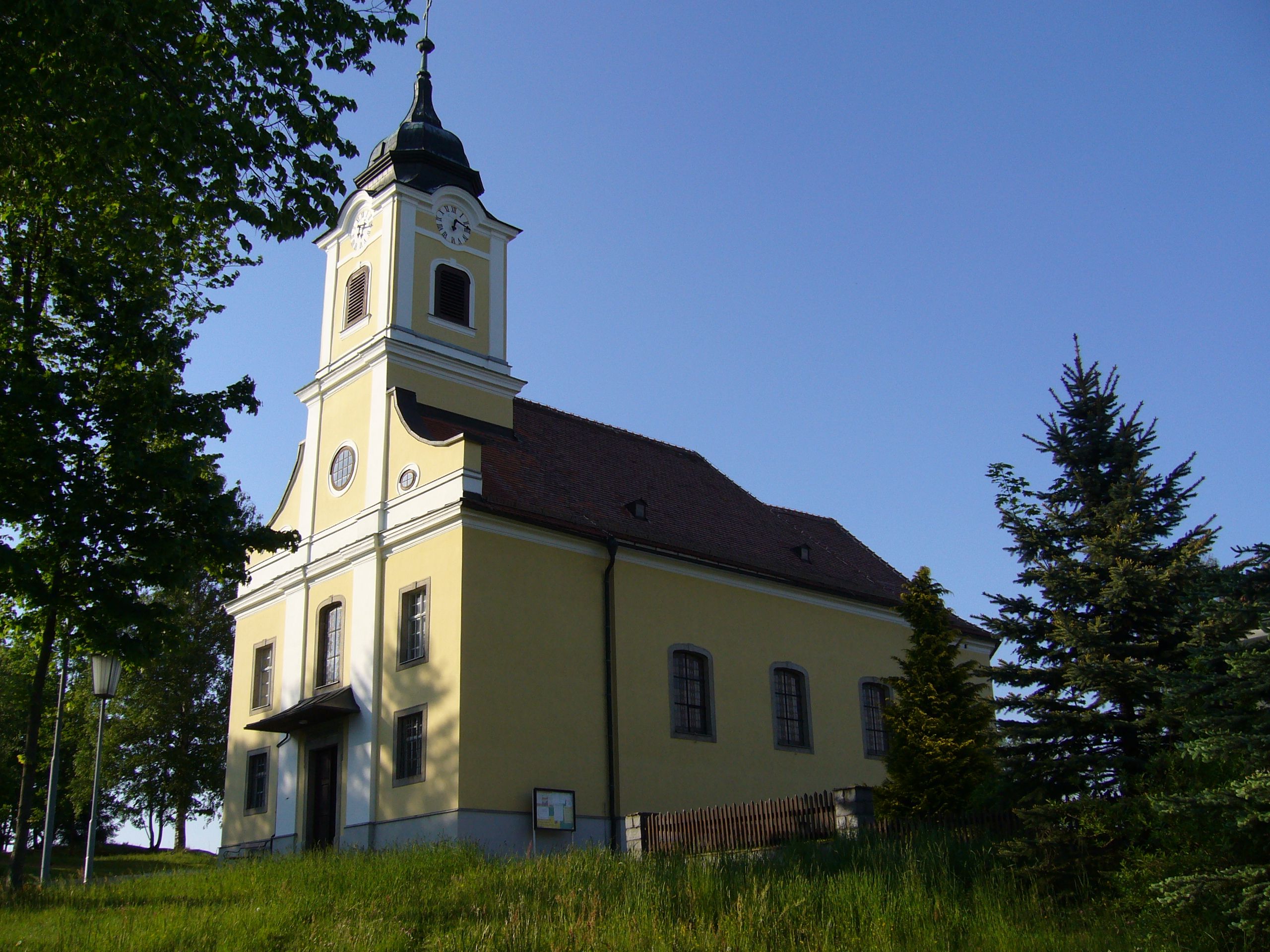 Pfarrkirche Haugschlag mit gelber Fassade und Turm, umgeben von Bäumen.
