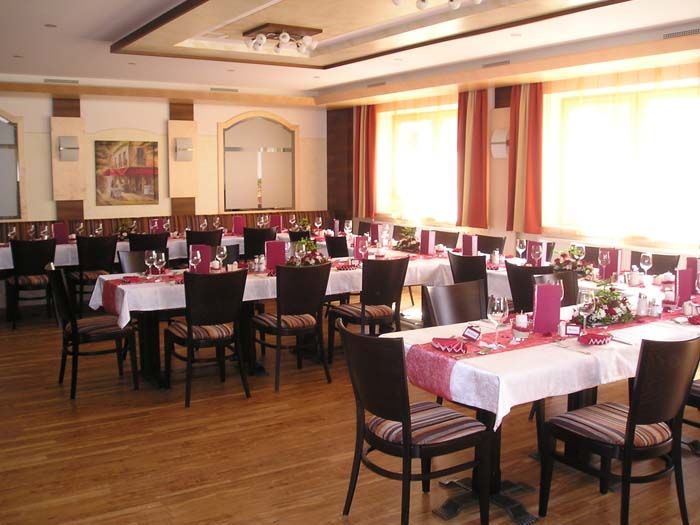 Ein elegant gedeckter Speisesaal mit mehreren Tischen, roten Tischläufern und Stühlen.