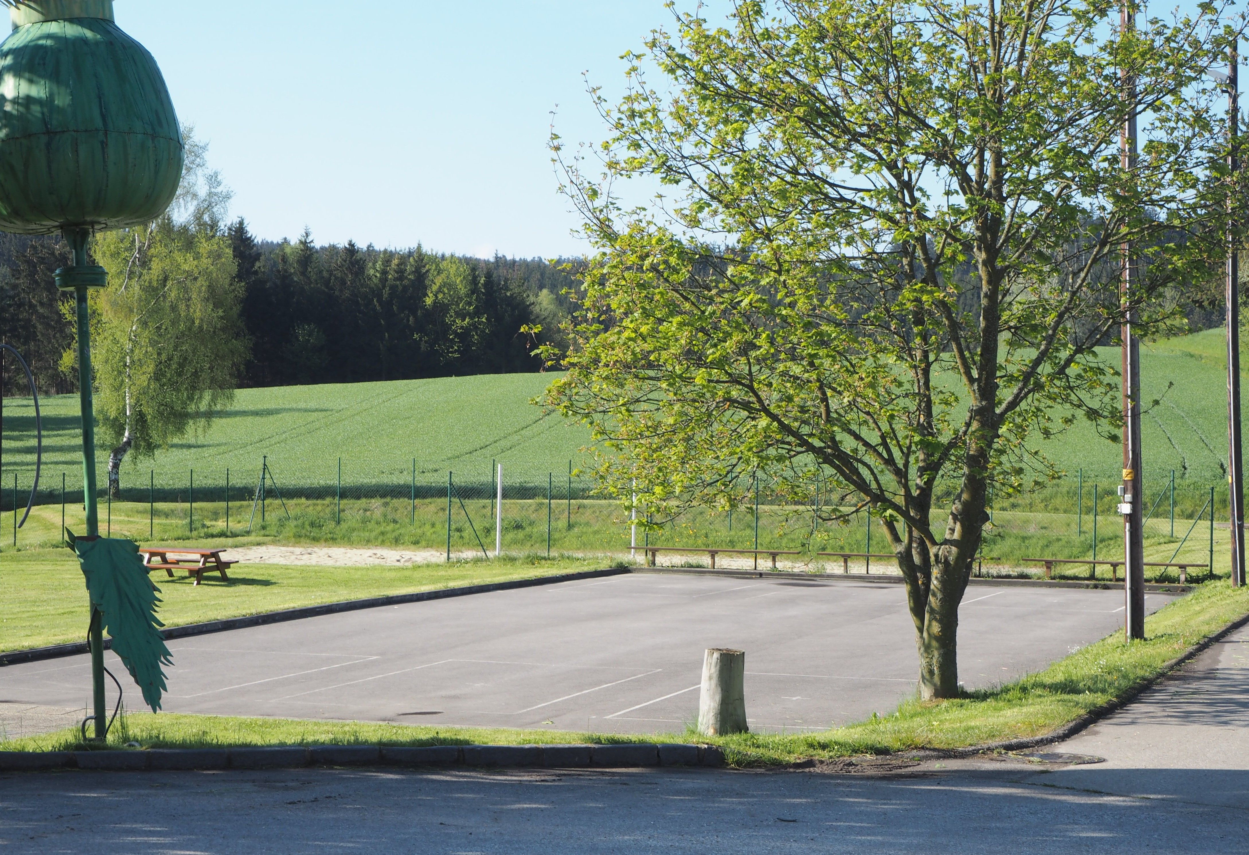 Asphaltplatz mit Baum und Volleyballfeld im Hintergrund.