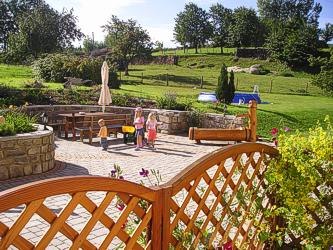Garten mit Terrasse, Spielplatz und grüner Wiese im Hintergrund.