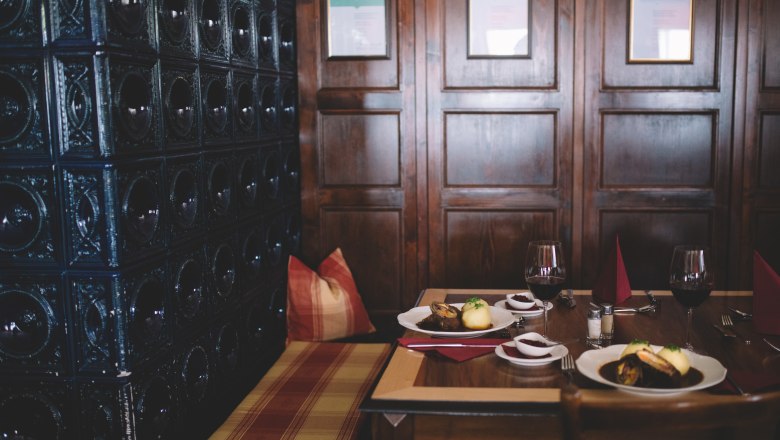 Cozy dining room with wooden walls, table setting and tiled stove.