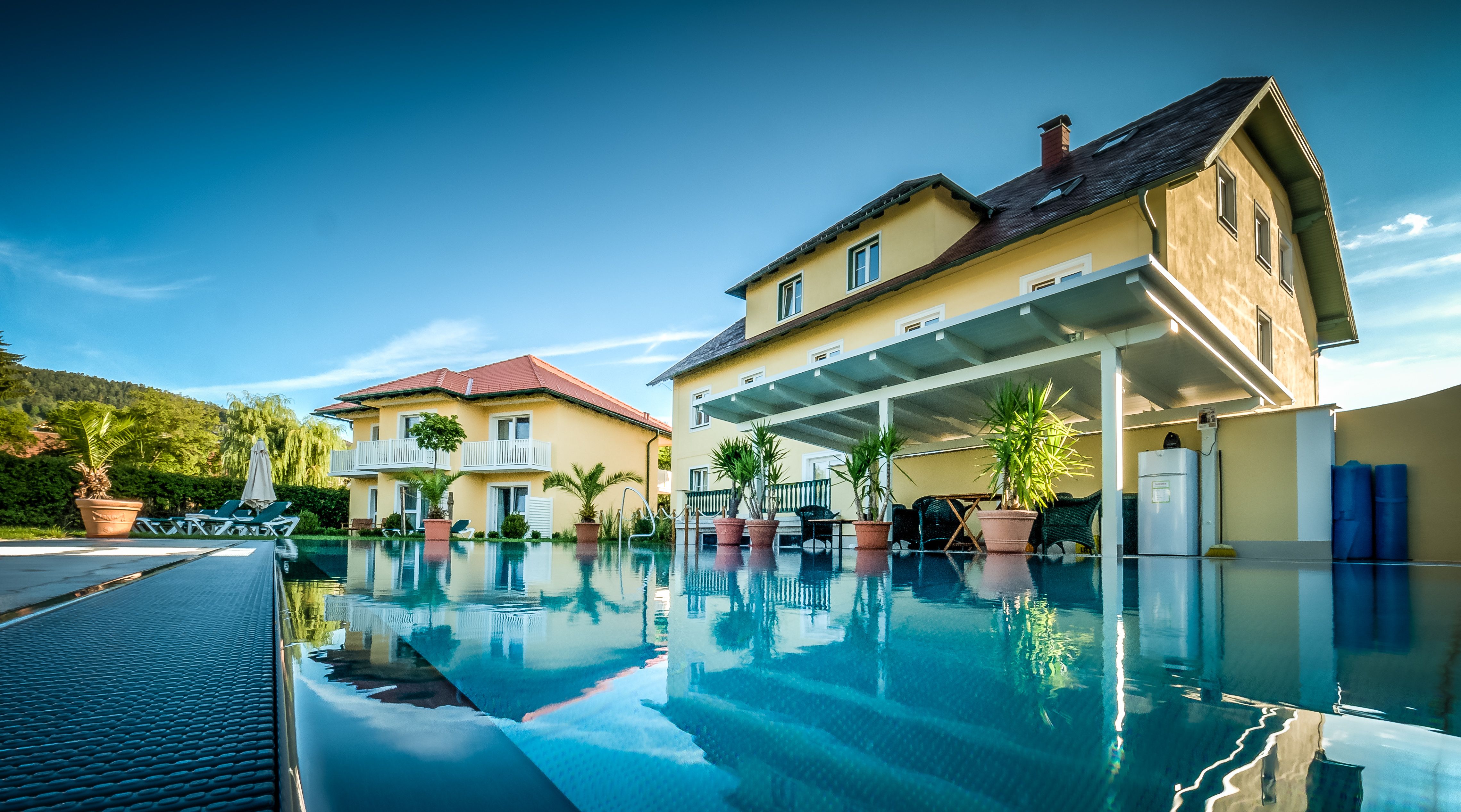 Die Gartenvilla mit großem Pool im Vordergrund, umgeben von Pflanzen und Liegestühlen.