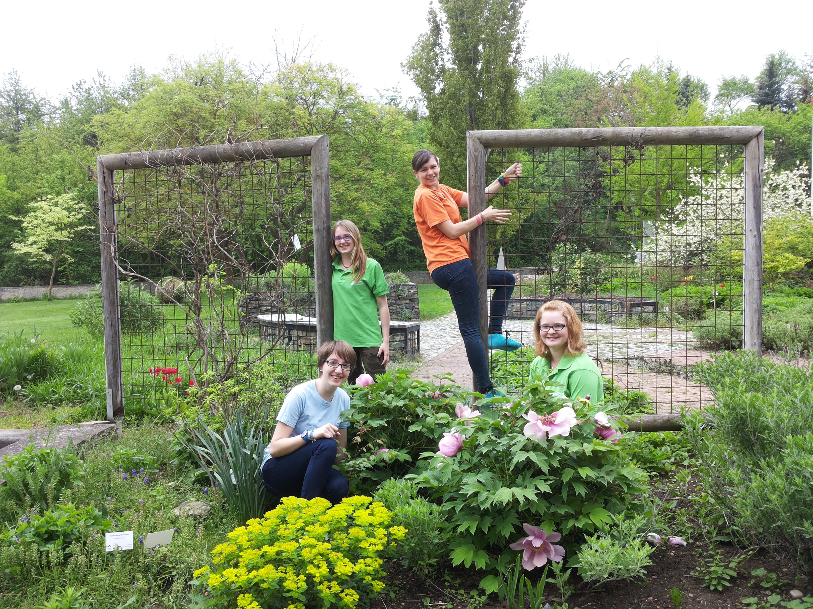 Vier Personen in einem Garten mit Blumen und Rankgittern.