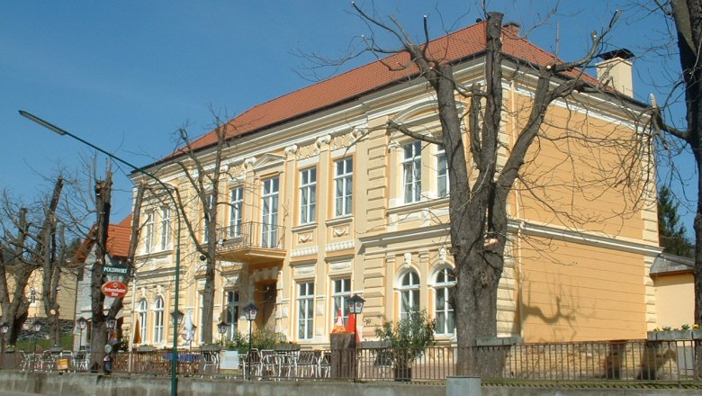 Gelbes Gebäude mit rotem Dach und kahlen Bäumen davor.