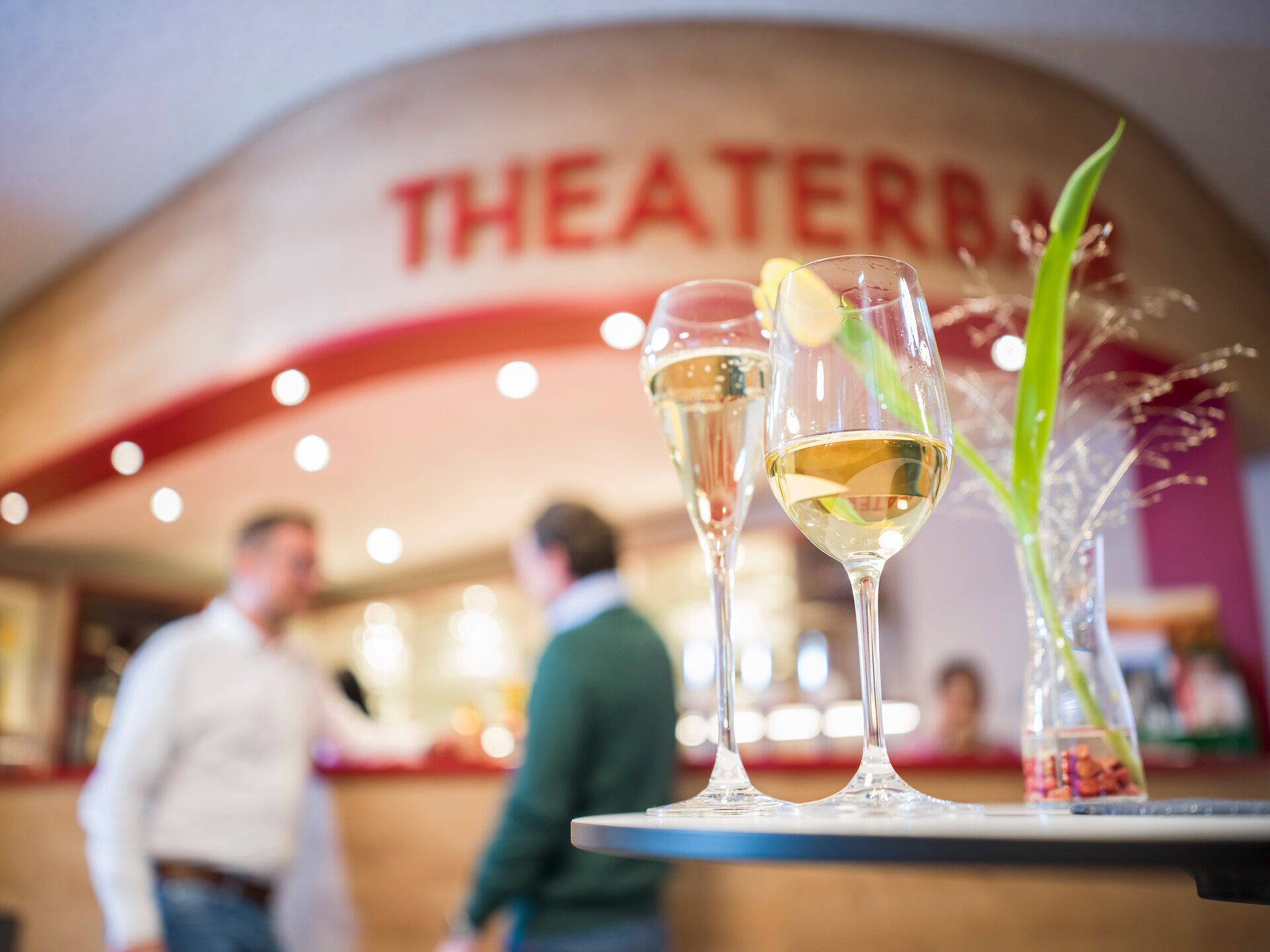 In der einladenden Atmosphäre der Theaterbar genießen Gäste prickelnde Getränke, während im Hintergrund angeregte Gespräche über die neuesten Kulturhighlights stattfinden. Die stilvolle Einrichtung und die sanfte Beleuchtung schaffen einen perfekten Ort, um den Abend zu verbringen und sich auf das bevorstehende Theaterstück zu freuen.