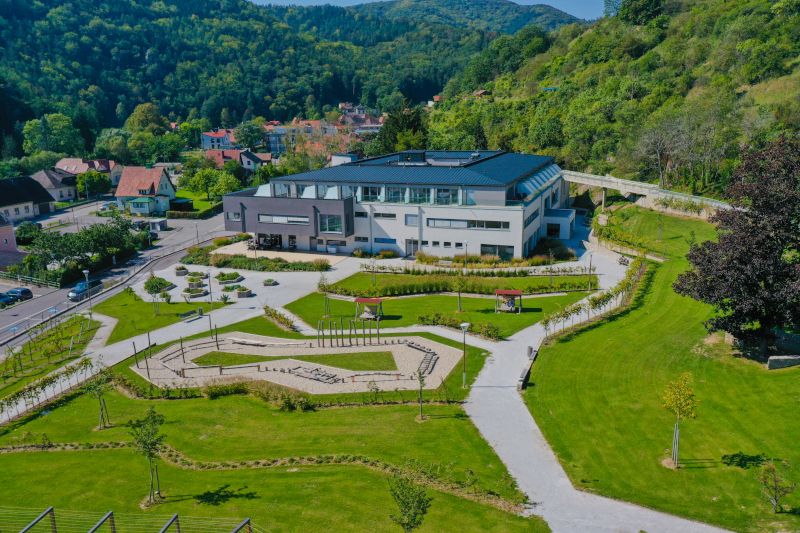 Luftaufnahme eines modernen Gebäudes mit Garten, umgeben von grünen Hügeln.