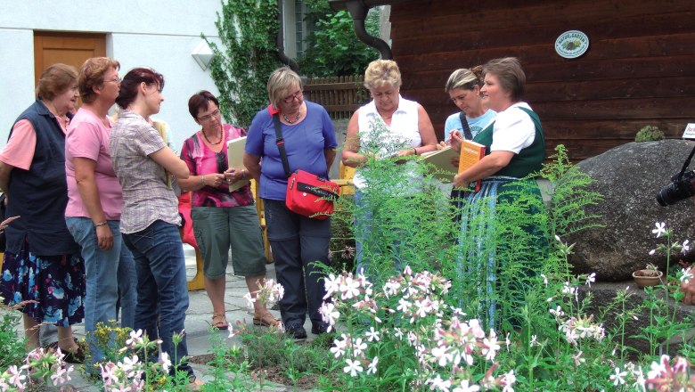Gruppe von Frauen in einem Kräutergarten, die einer Führung lauschen.