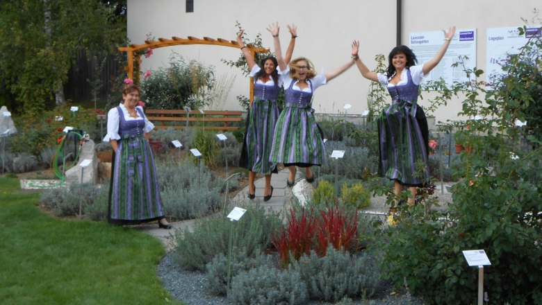 Frauen in Dirndln springen in einem Lavendelfeld.