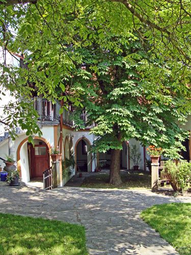 Ein idyllischer Innenhof mit einem großen Baum, umgeben von einem Gebäude mit Arkaden und Balkonen.