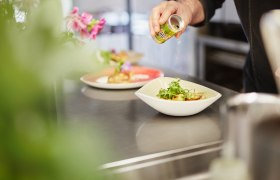 Ein Koch w&uuml;rzt ein Gericht in einer Sch&uuml;ssel mit Kr&auml;utern aus einer kleinen Dose.