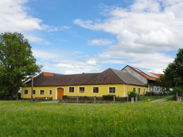 Gelbes Bauernhaus auf einer grünen Wiese mit blauem Himmel und Wolken.
