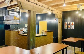 Innenansicht eines modernen Caf&eacute;s mit Holzbalken, Bartresen und hohen Tischen.