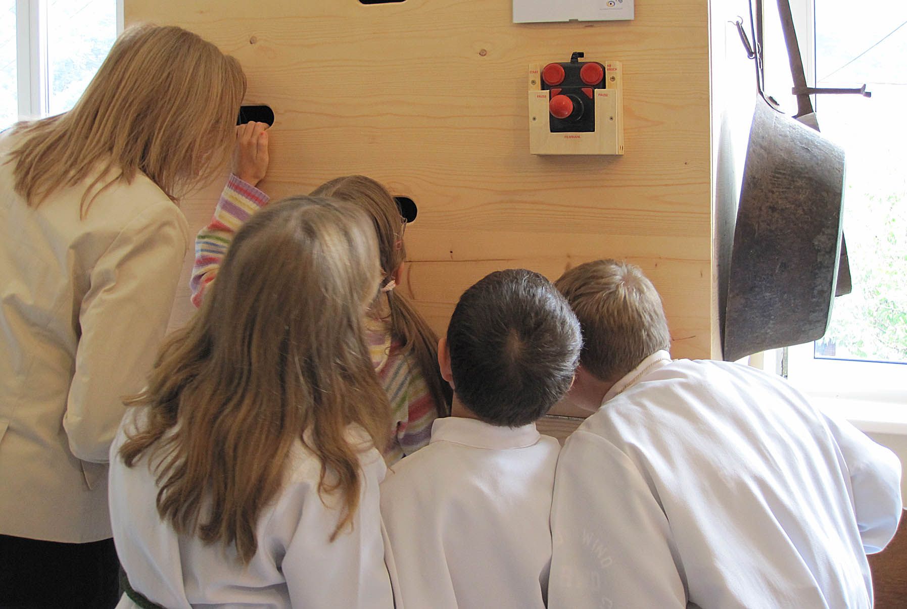 Gruppe von Kindern und einer Frau schauen durch Löcher in einer Holzwand.