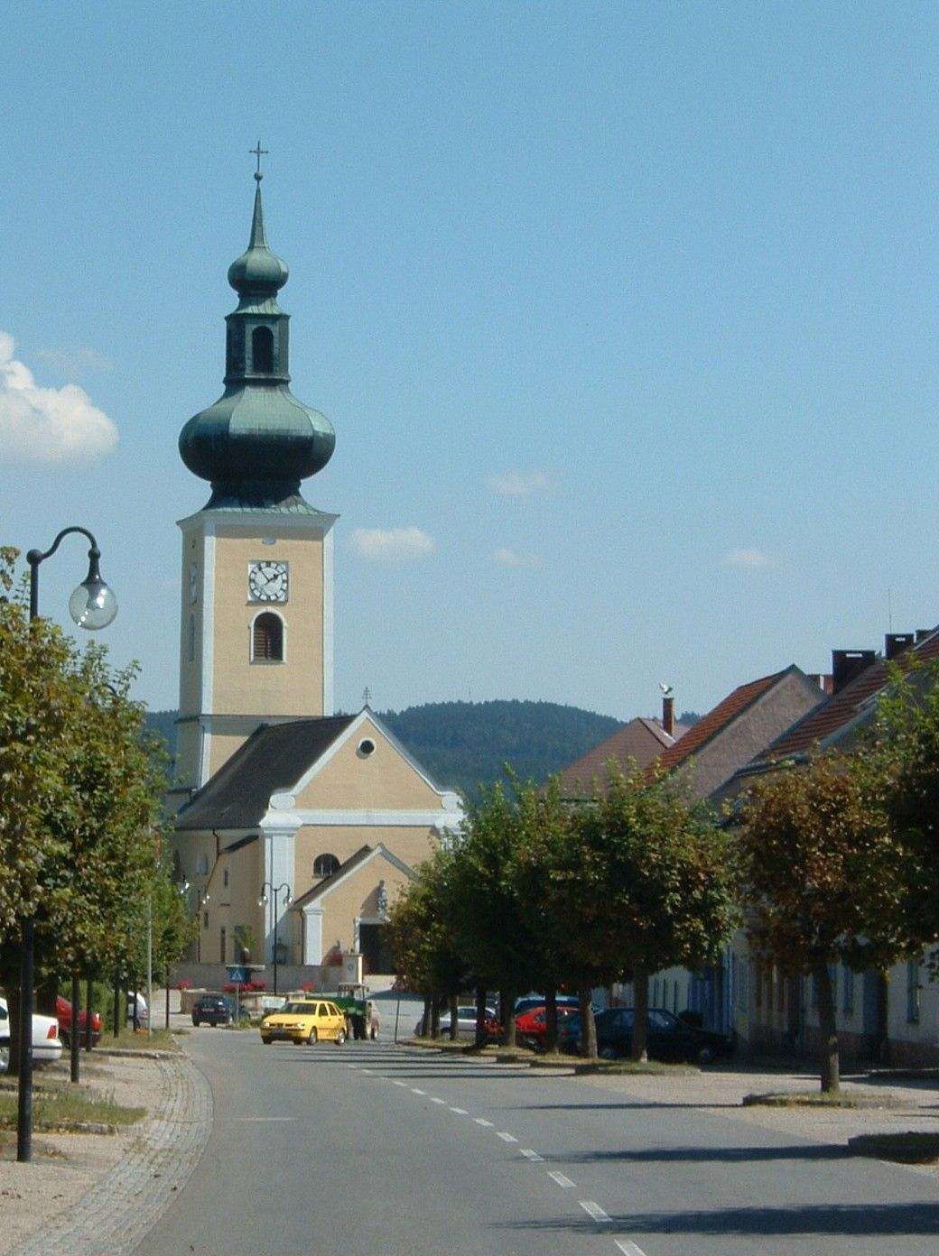 Kirche mit Zwiebelturm in einer kleinen Stadt, umgeben von Bäumen und Häusern.